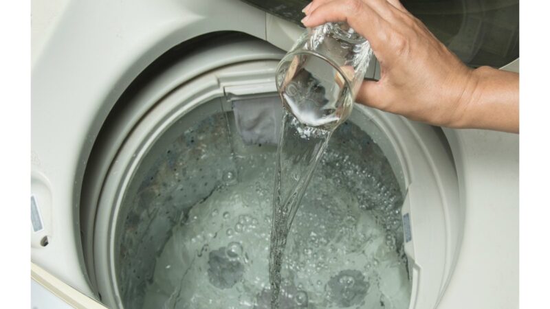 Bottiglia di aceto bianco accanto a una lavatrice moderna.