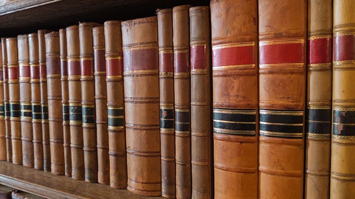 Biblioteca con libri antichi su scaffali in legno ben illuminati.