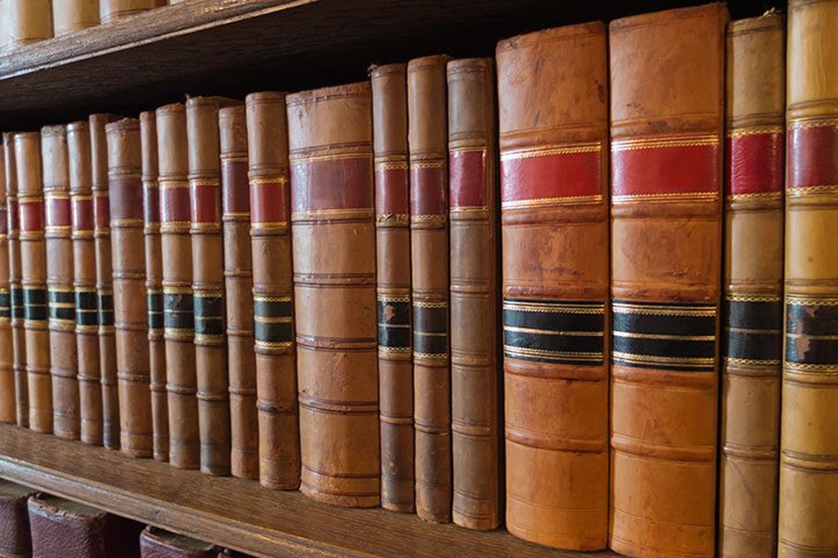 Biblioteca con libri antichi su scaffali in legno ben illuminati.