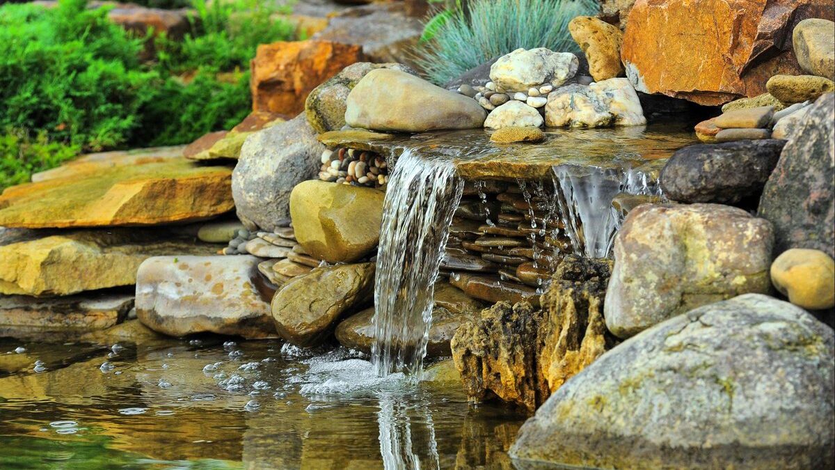 Cascata da giardino fai-da-te con pietre naturali e piante verdi.