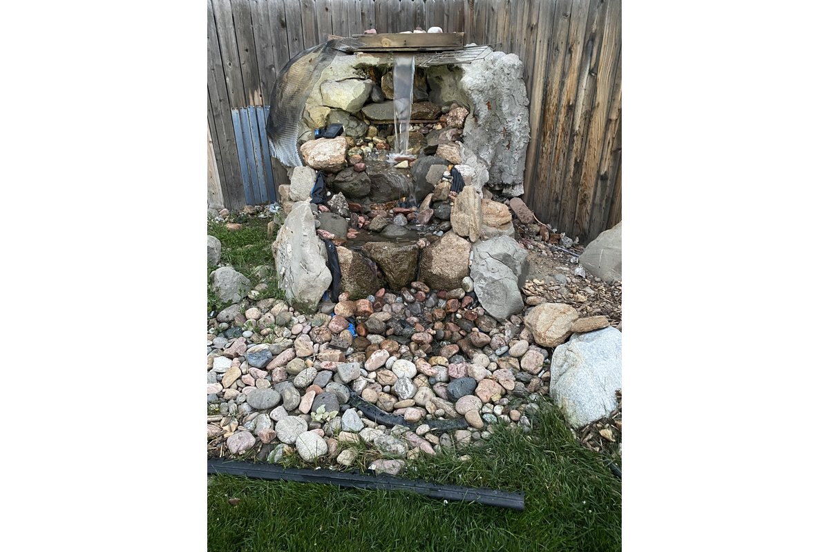 Cascata da giardino fai-da-te con pietre e vegetazione rigogliosa.