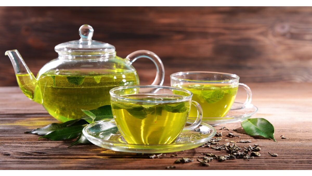 Tazza di tè verde fumante su un tavolo di legno con foglie di tè.