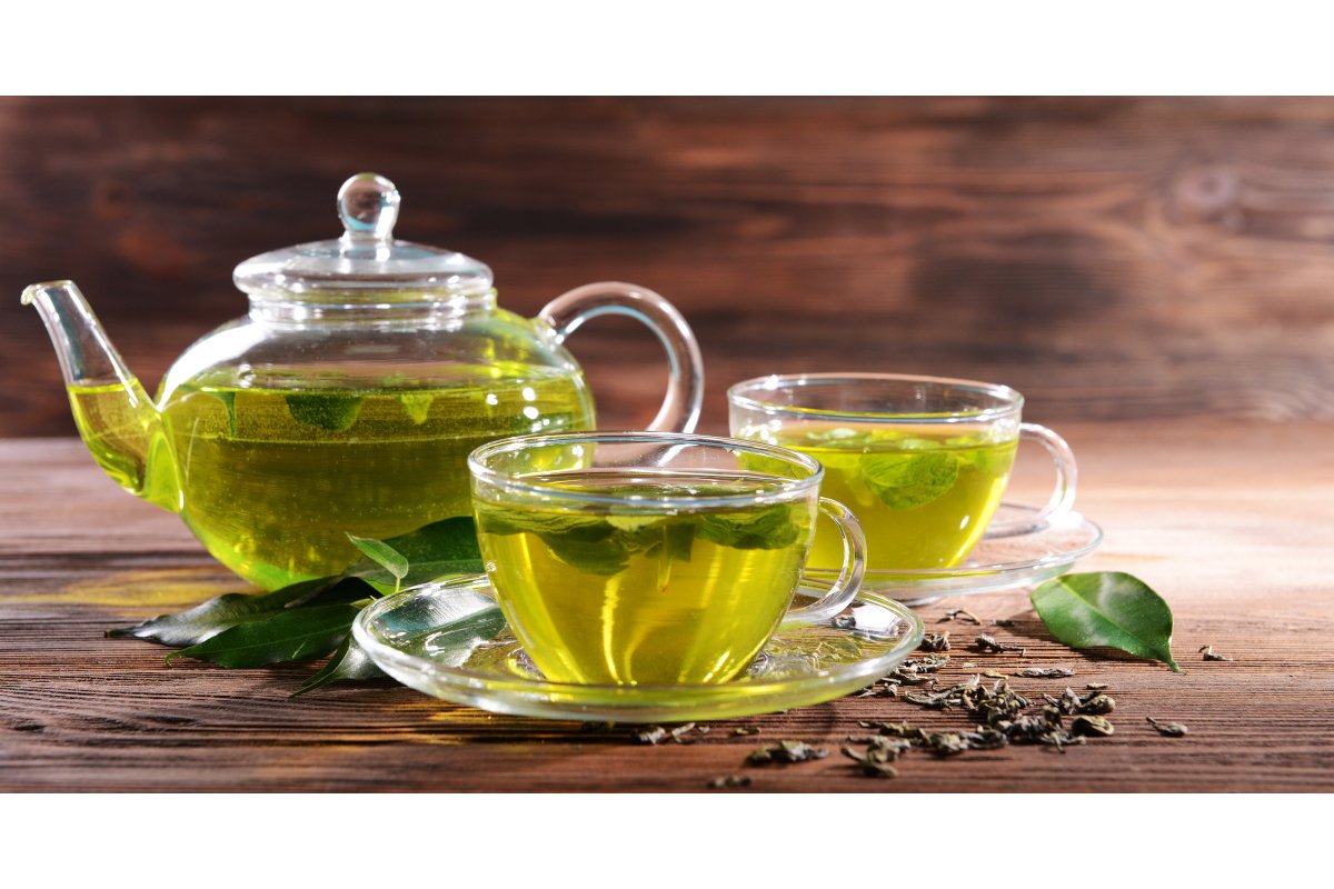 Tazza di tè verde fumante su un tavolo di legno con foglie di tè.