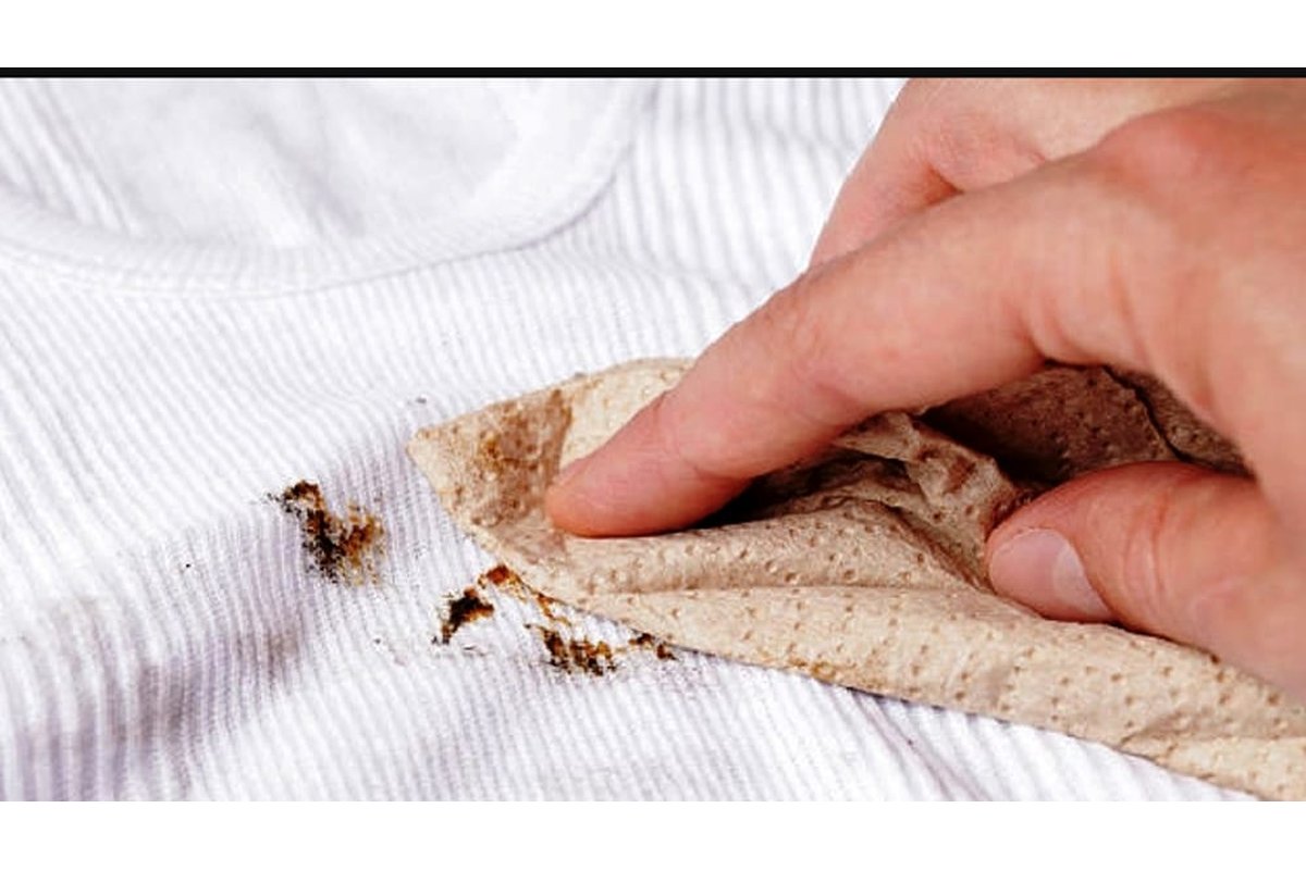 Mano che applica rimedio naturale su macchia di tessuto chiaro.