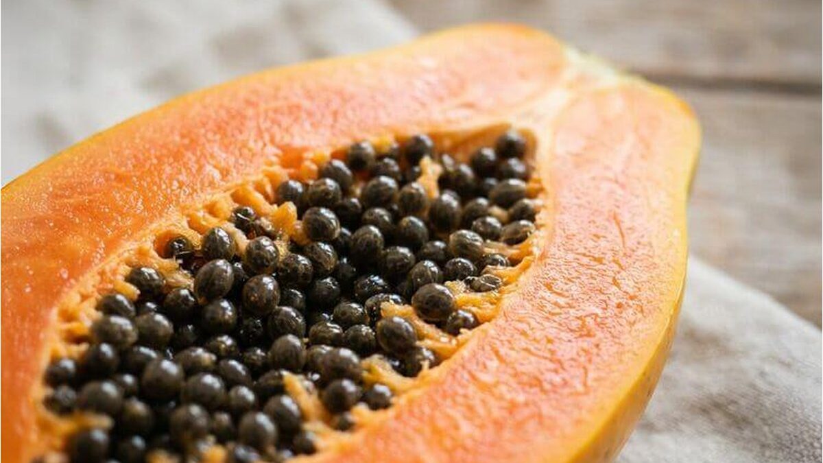 Donna sorridente che tiene una papaya matura in cucina luminosa.