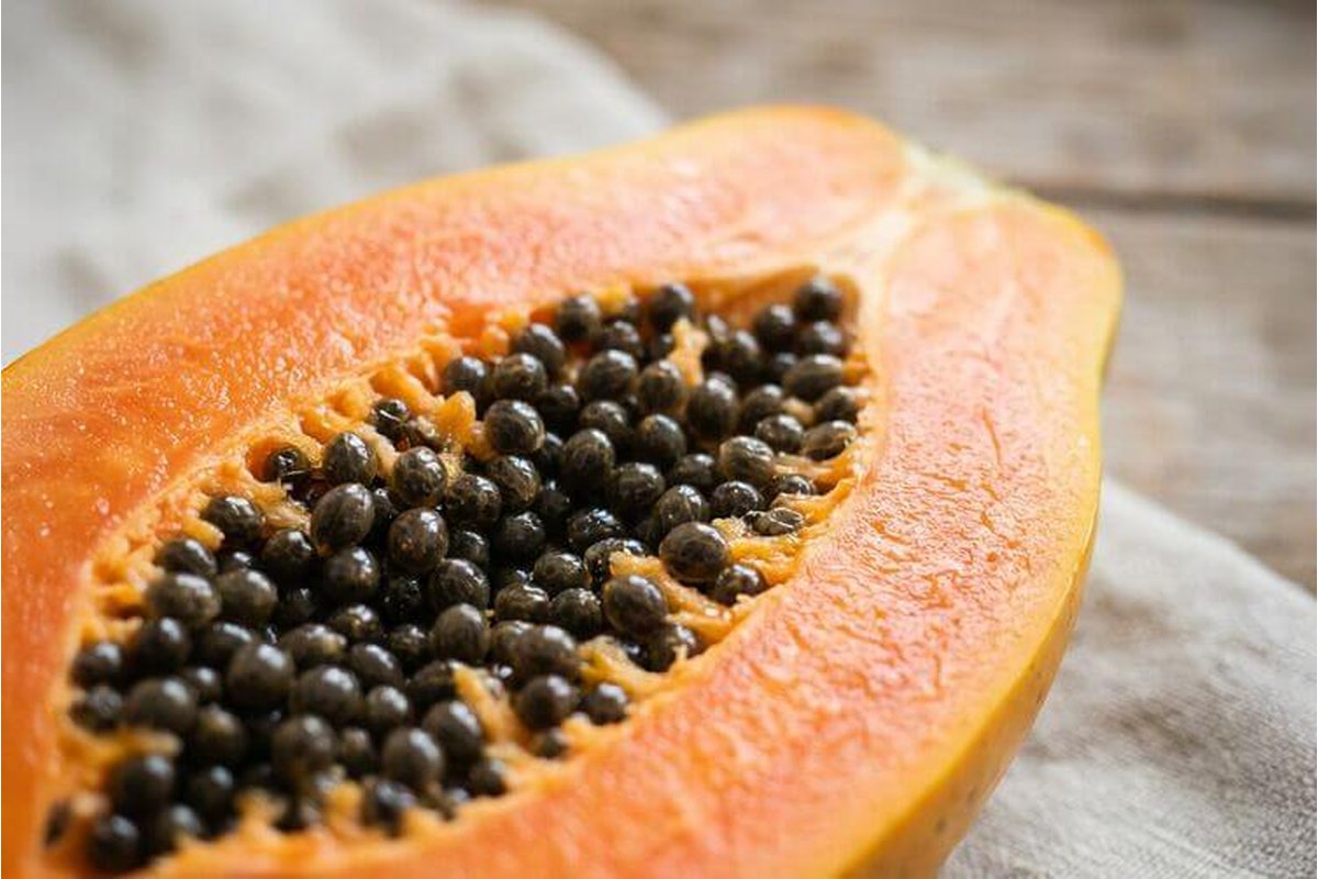 Donna sorridente che tiene una papaya matura in cucina luminosa.