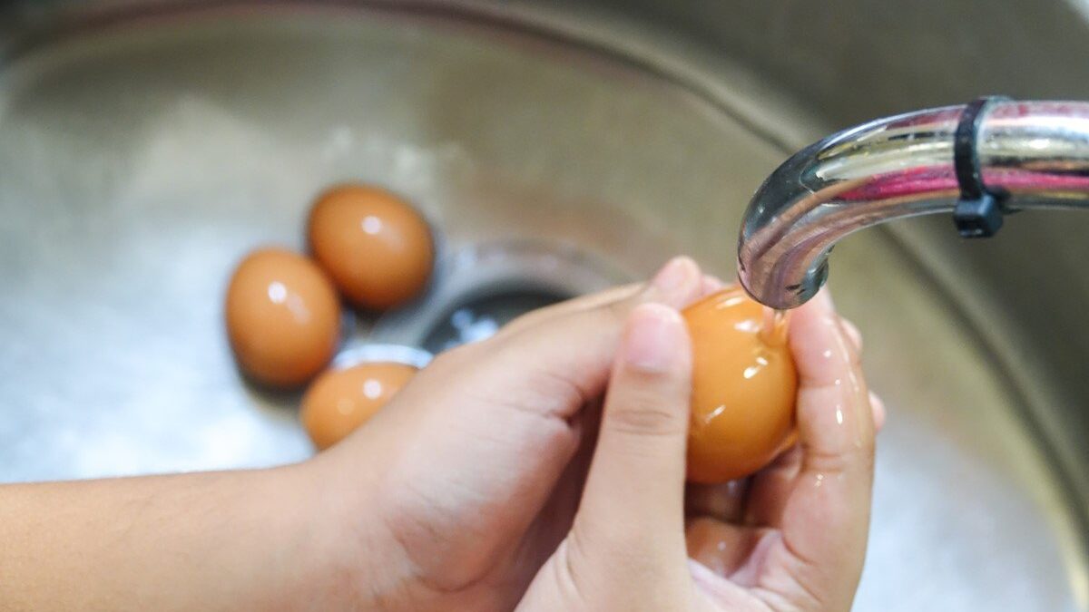 Mani che lavano un uovo sotto l'acqua corrente del rubinetto.