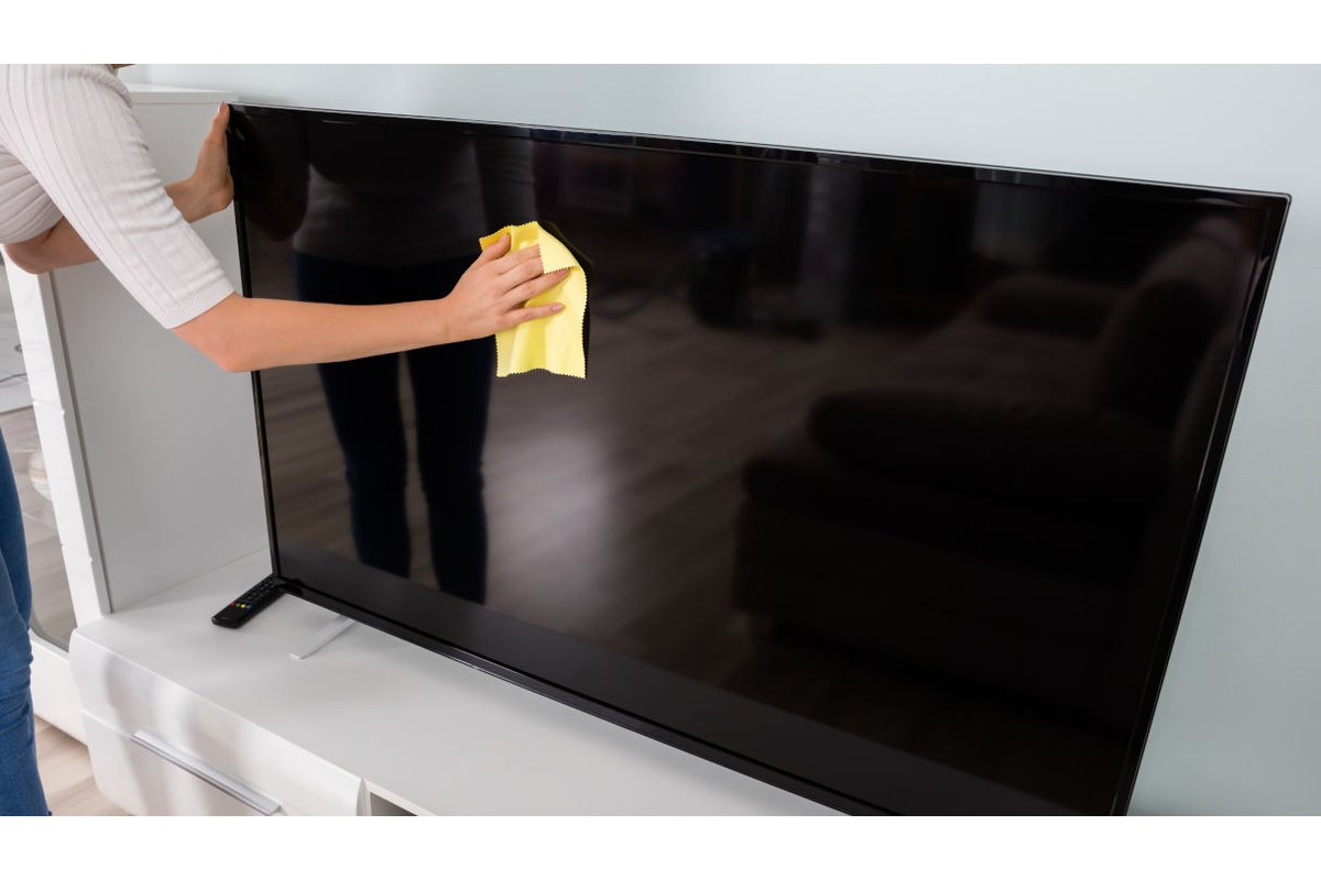 Persona pulisce lo schermo della TV con un panno morbido.